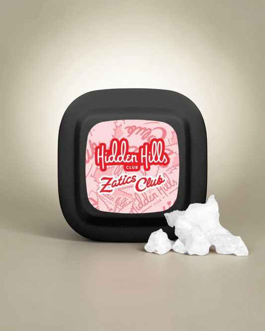 Concentrado Hidden Hills Club Zatics en envase negro mate con etiqueta rosa y cristales blancos sobre mesa de madera